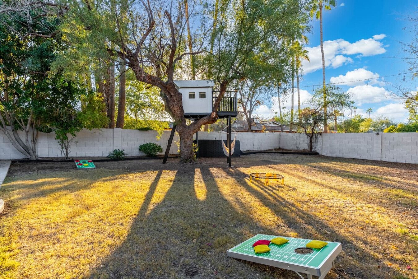 A treehouse attached to a tree in a backyard with a trampoline and a small play area.
