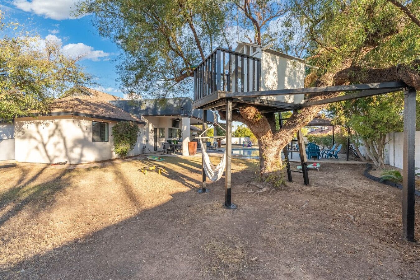 A playground with a swing set and a climbing structure, surrounded by trees and a white building.