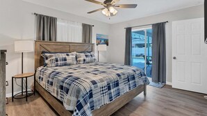Ein Schlafzimmer mit einem Bett, einem Deckenventilator, einer Lampe und Blick ins Freie.