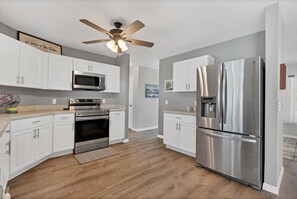 A modern kitchen with white cabinets, stainless steel appliances, a ceiling fan, and a wooden floor. - Dbd1014 (Port Charlotte)