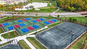 A tennis court complex with multiple courts, a parking area, and a surrounding landscaped area with trees and a pond. - Hlb14131-828 (Punta Gorda)