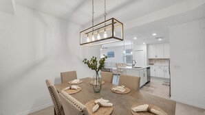 A modern dining area with a wooden table, woven placemats, and a glass vase with greenery. - Hlb14131-828 (Punta Gorda)
