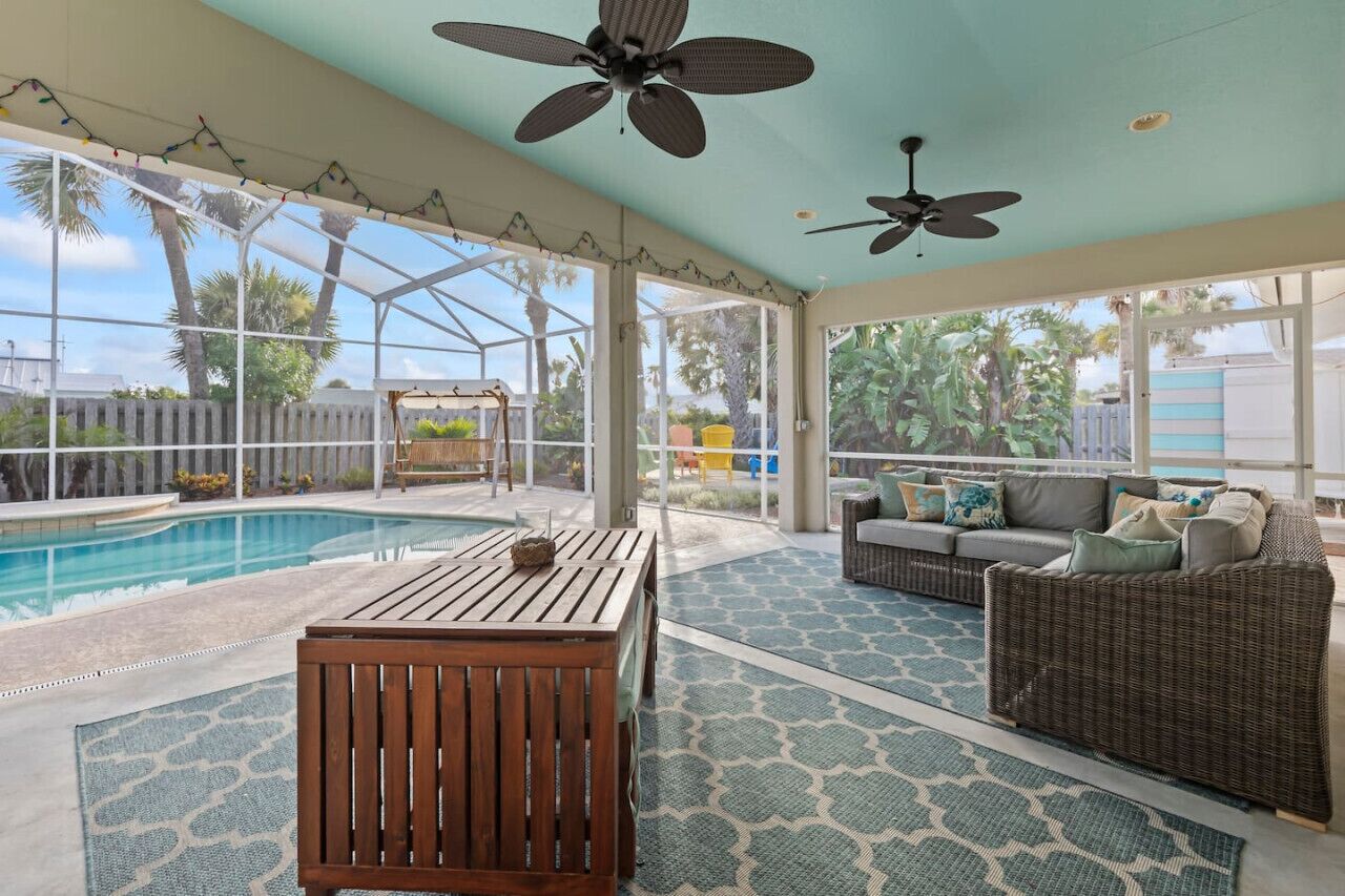 A covered outdoor area with a pool, seating, and ceiling fans.