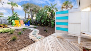A wooden deck with a garden area, including a pathway, colorful chairs, and various plants. - Sandcastle Harbor Pool & Firepit Steps to the Beach! (Ponce Inlet)