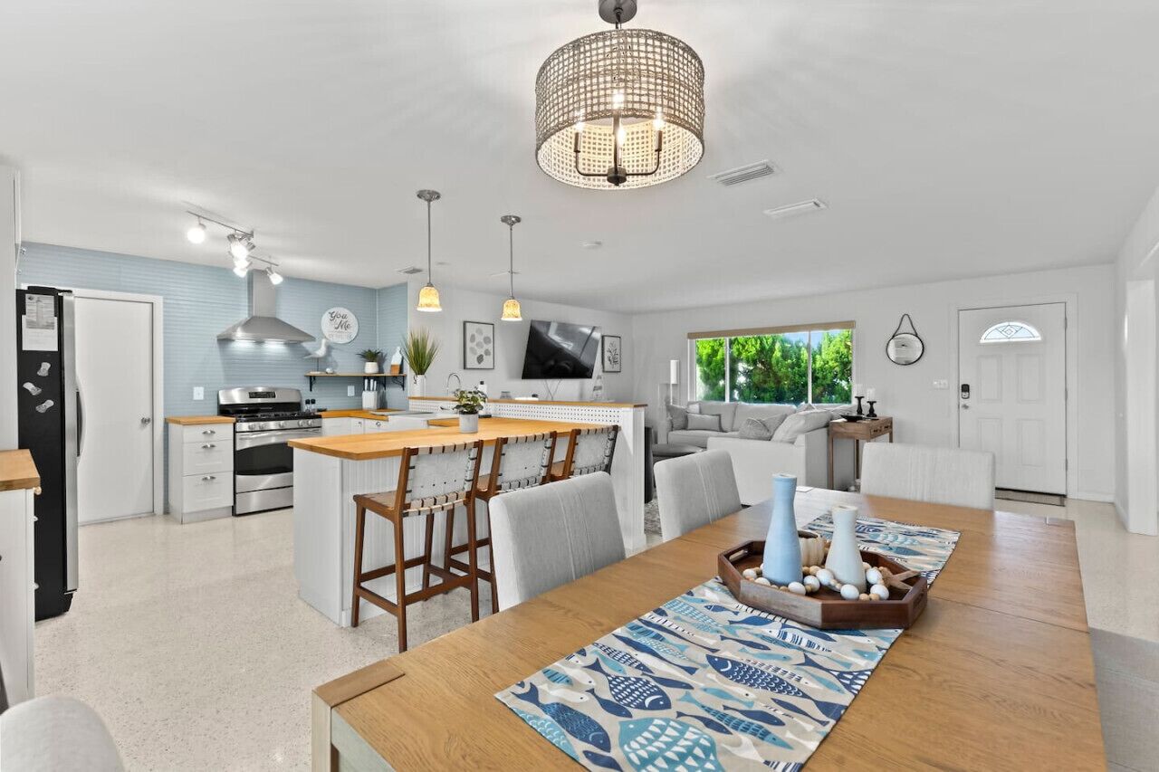 Een moderne keuken met een centraal eiland, een eethoek met een houten tafel en stoelen, en een woonruimte met een bank en een televisie.