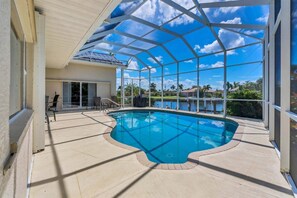 Una piscina con cerramiento de vidrio, rodeada por un patio con sillas y una zona de estar cubierta.