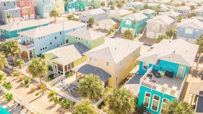 A residential area with colorful houses, a gated entrance, and a small patio area with outdoor furniture. - Bach Porch - Beach Gear Credit Included! 2 Shared Heated Pools! (Port Aransas)