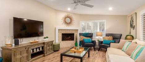 A living room with a television, fireplace, ceiling fan, and seating area.