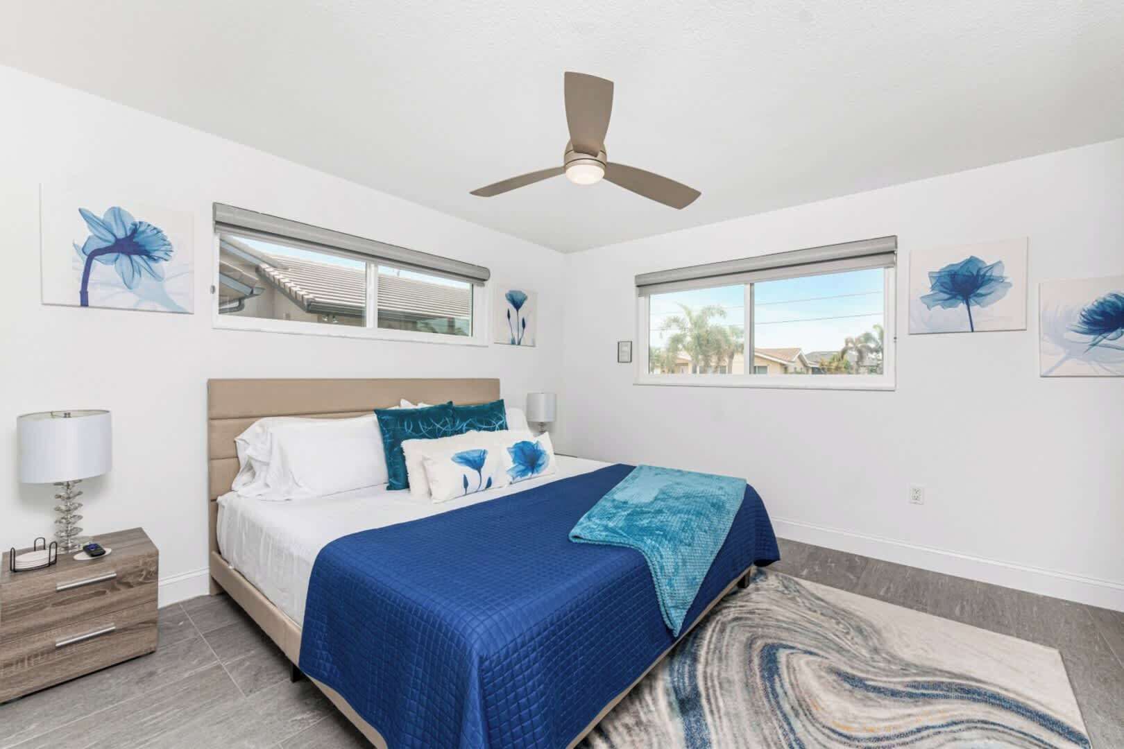 A bedroom with a bed, a nightstand, a lamp, a ceiling fan, and artwork on the walls.