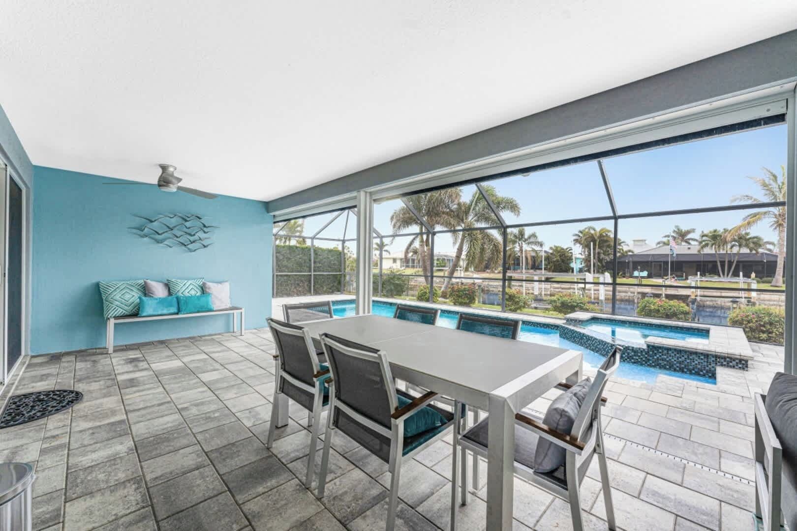 A modern outdoor patio with a pool, a dining table, and a seating area with a blue wall and decorative wall art.