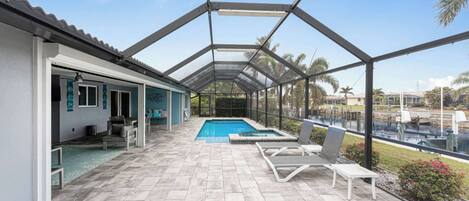 A covered outdoor swimming pool area with lounge chairs and a patio.