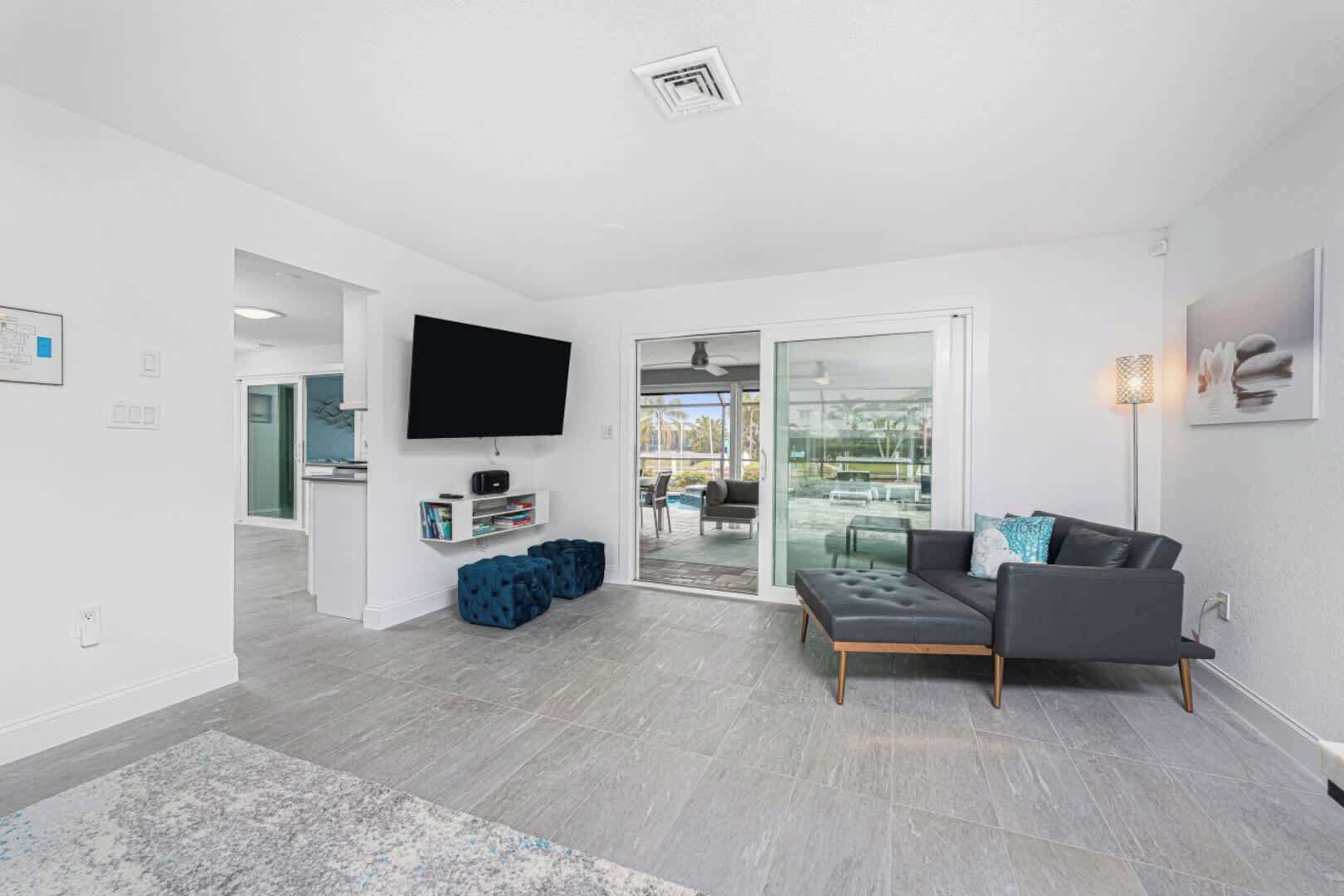 A modern living room with a grey sofa, a flat-screen TV, and a glass door leading to a balcony.