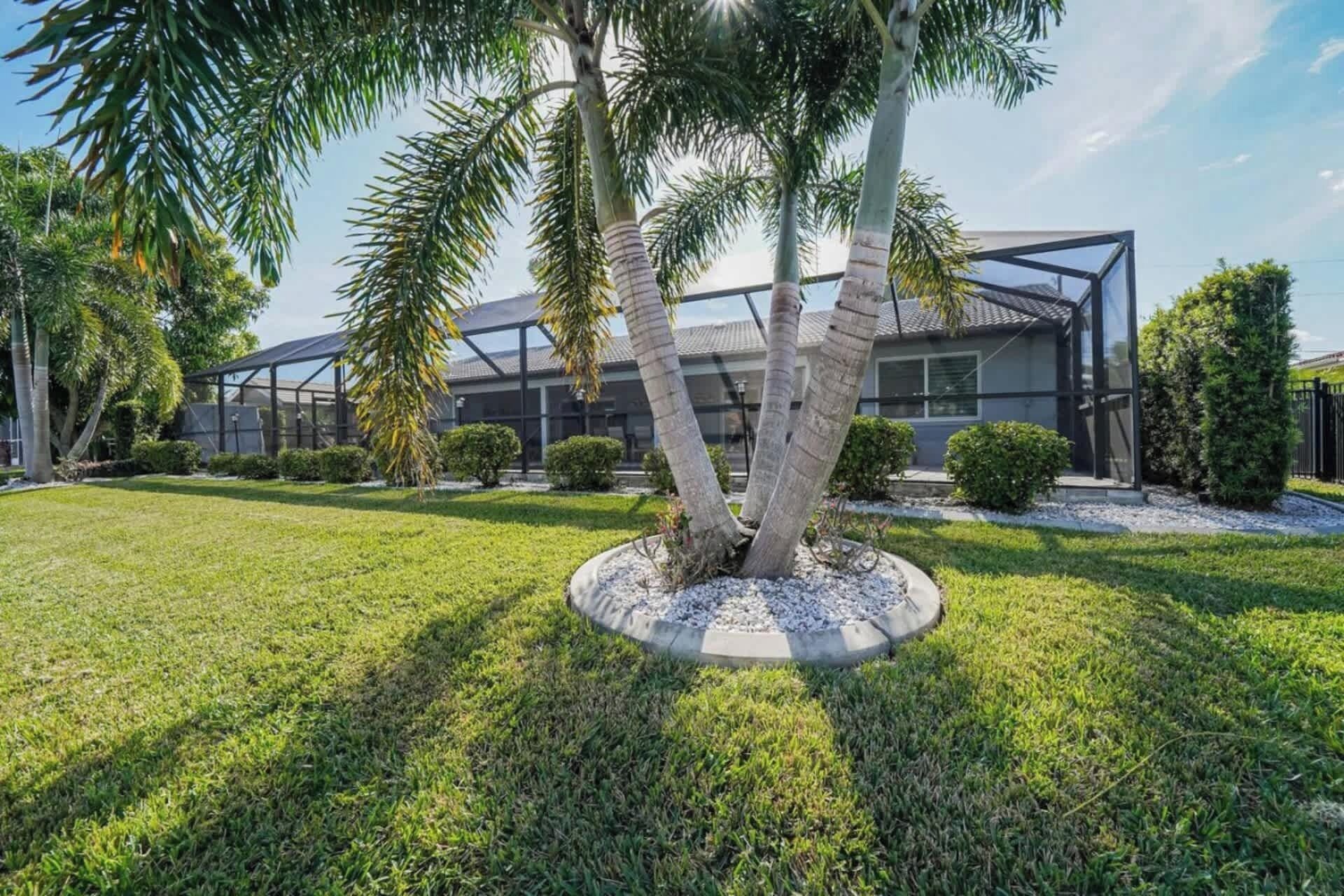 Un edificio moderno con fachada de vidrio y un césped cuidado con palmeras.