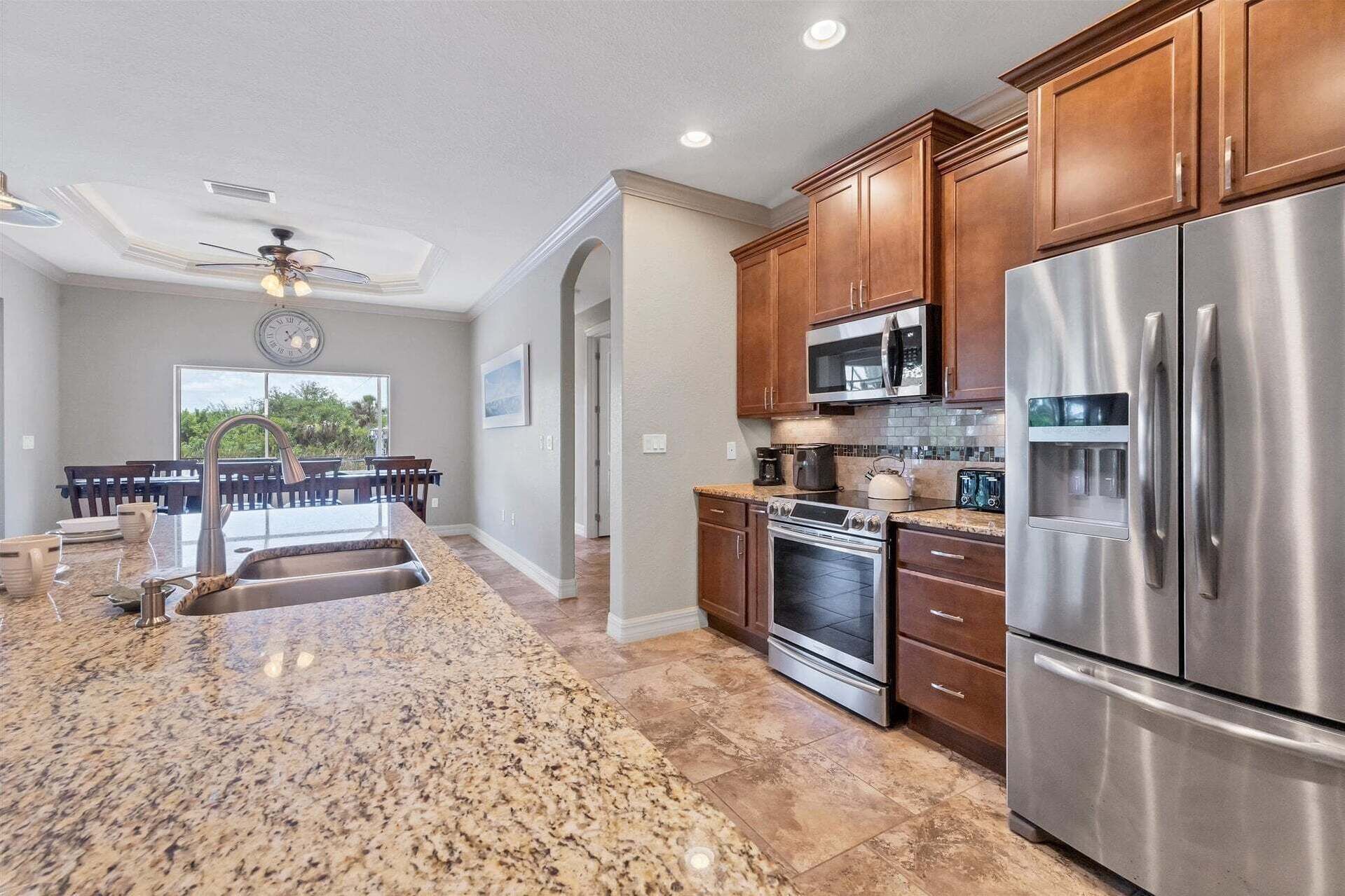 A kitchen with granite countertops, stainless steel appliances, wooden cabinets, and a dining area with a table and chairs.