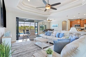 A spacious living room with a sofa, coffee table, and a dining area with chairs. There is a kitchen area with modern appliances and a ceiling fan. - Myc14422 (Port Charlotte)
