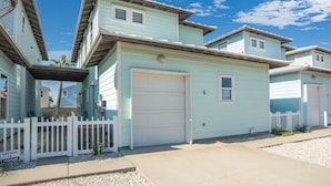 Uma fileira de casas móveis azul claro com portas de garagem brancas, um cercado branco de piquetes e um céu azul límpido.