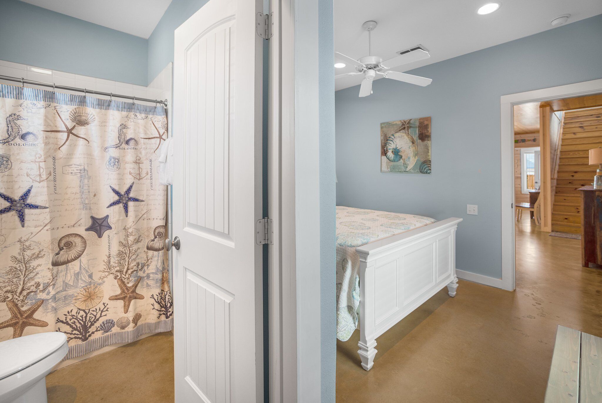 A bathroom with a nautical-themed shower curtain, a white toilet, and a wooden floor.