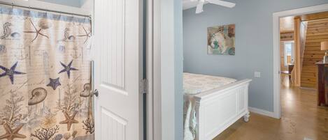 A bathroom with a nautical-themed shower curtain, a white toilet, and a wooden floor.