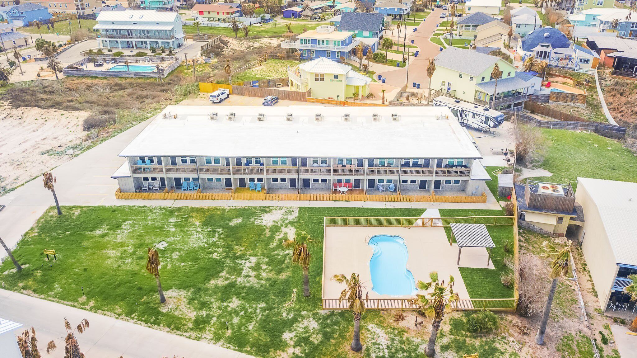 Un edificio de dos pisos con techo plano, piscina y patio cercado.