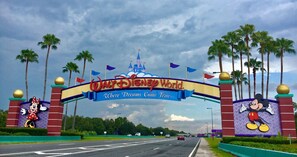 Η είσοδος στο Walt Disney World, με μια μεγάλη πινακίδα που απεικονίζει τον Μίκυ Μάους και την Μίνι Μάους, φοίνικες και ένα κάστρο στο βάθος.