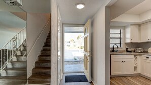 A modern kitchen with white cabinets, a wooden staircase, and a view to the outside. - Yellow Sunshine Oceanfront Townhouse, Private Balcony Unit #2 (Ponce Inlet)