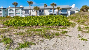A beachfront hotel with multiple-story buildings, palm trees, and a sandy path leading to the entrance. - Yellow Sunshine Oceanfront Townhouse, Private Balcony Unit #2 (Ponce Inlet)