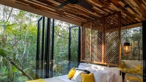 A bedroom with a bed, yellow pillows, and a view of the forest through large windows. - Cube House (Tulum)