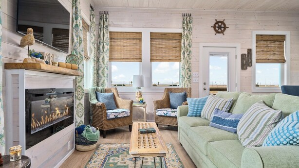 A cozy living room with a fireplace, wicker furniture, and a view of the beach. - St Jo's Bungalow (Port Aransas)
