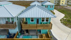A beachfront property with multiple buildings, a wooden deck, and a swimming pool. - St Jo's Bungalow (Port Aransas)