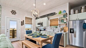 A kitchen with a wooden table, chairs, and a stainless steel refrigerator. - St Jo's Bungalow (Port Aransas)