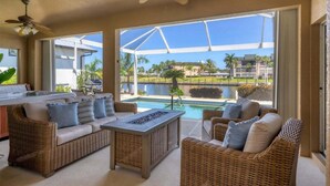 A sunlit patio with wicker furniture, a pool, and a view of a water body and buildings. - Gic120 (Punta Gorda)