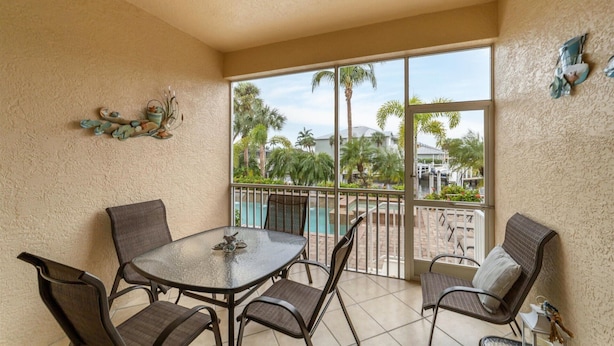A balcony with a glass table and chairs, a view of a pool and palm trees, and decorative wall art. - Ppm3329-112 (Punta Gorda)