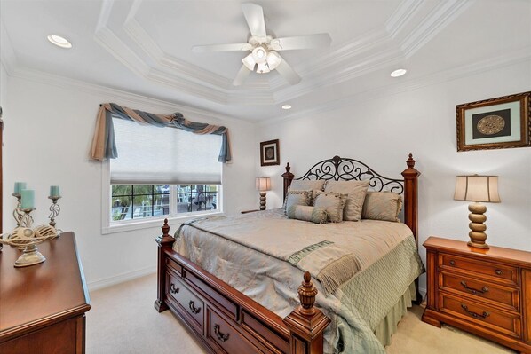 A bedroom with a bed, a dresser, a nightstand, a ceiling fan, and a window with blinds.