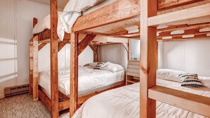 Ein Schlafraum mit Etagenbetten, Holzbalken, weißer Bettwäsche und einem kleinen Nachttisch mit Radio.