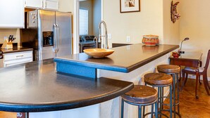 A modern kitchen with a central island, bar stools, pendant lighting, and stainless steel appliances. - Western Star Ahwatukee (Phoenix)