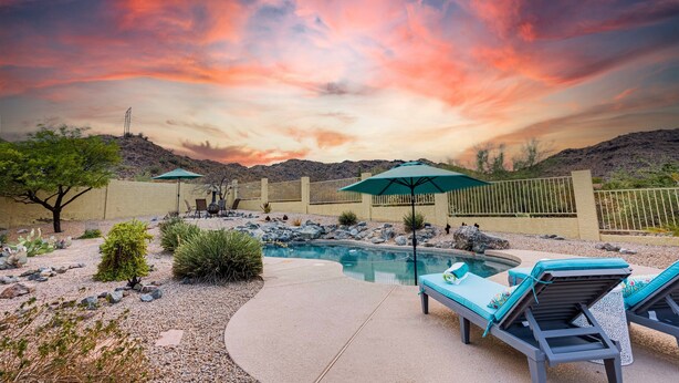A pool area with lounge chairs and umbrellas, surrounded by a landscaped garden and a view of the mountains. - Western Star Ahwatukee (Phoenix)