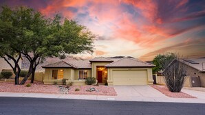 A single-story house with a red door and beige siding, surrounded by a landscaped garden with red gravel and a small tree. - Western Star Ahwatukee (Phoenix)
