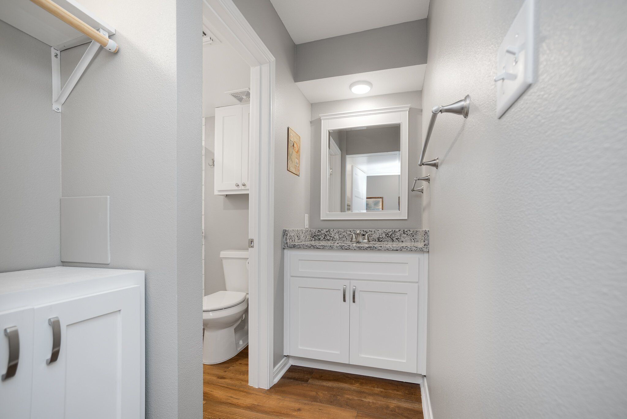 Un baño con muebles blancos, encimera de granito y un espejo sobre el lavamanos.