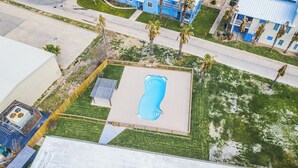 Ein Luftbild eines Wohngebiets mit Schwimmbad, umzäunter Garten und einem blauen Gebäude im Hintergrund.