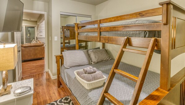 Un lit superposé avec une structure en bois, une couette grise et un panier contenant des serviettes.