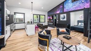 Eine moderne Wohnung mit Küche, Wohnbereich und einer Wand mit einem Wandbild zum Thema Galaxie.