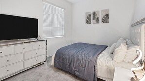Ein Schlafzimmer mit einem Bett, einem Schminktisch, einem Flachbildfernseher, einem Deckenventilator und Wandbildern.