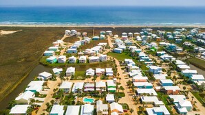 An aerial view of a coastal residential area with houses, a beach, and a body of water. - Casa Las Palmas - Boardwalk to the Beach! (Port Aransas)