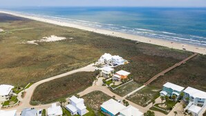 An aerial view of a coastal property with multiple buildings, a beach, and a pier. - Casa Las Palmas - Boardwalk to the Beach! (Port Aransas)