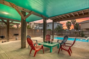 An outdoor patio with a pool, wooden deck, and a covered seating area with chairs. - Boogie Board Bungalow - Pet Friendly! Private Pool! 2 (Port Aransas)