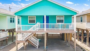 A turquoise two-story house with a balcony, wooden deck, and a visible door number. - Boogie Board Bungalow - Pet Friendly! Private Pool! 2 (Port Aransas)