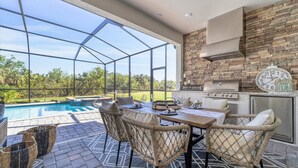 An outdoor patio with a pool, wicker furniture, a grill, and a stone wall. - Cbw14724 (Punta Gorda)