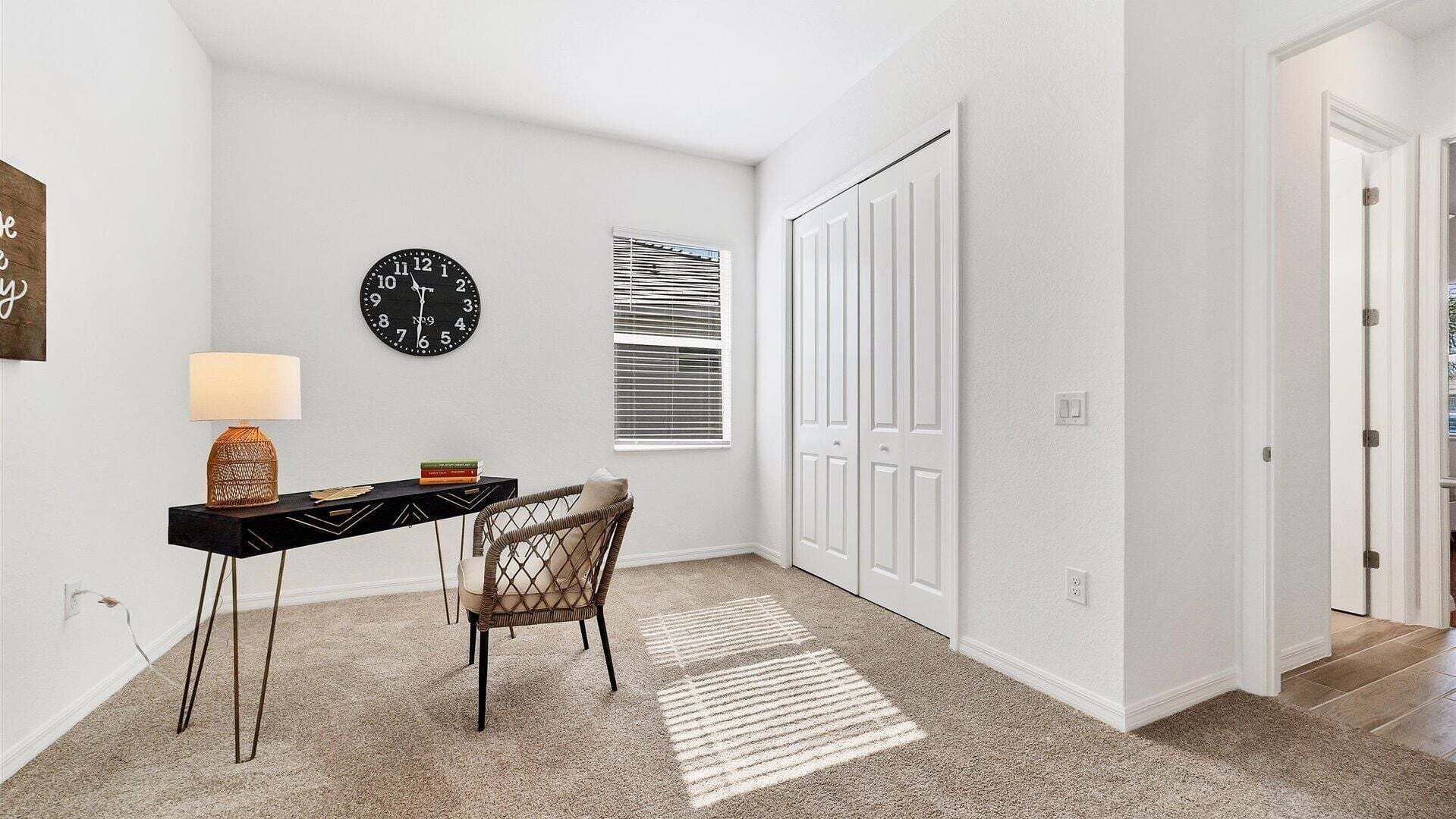 A hallway with a clock, a lamp, a chair, and a door.