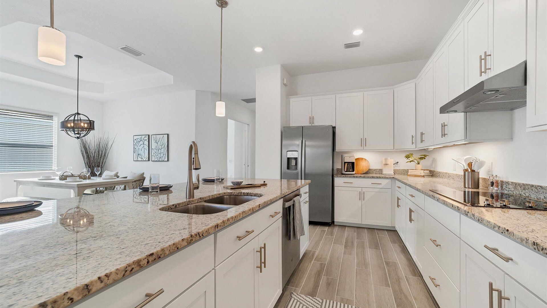 A modern kitchen with white cabinetry, granite countertops, stainless steel appliances, and pendant lighting.