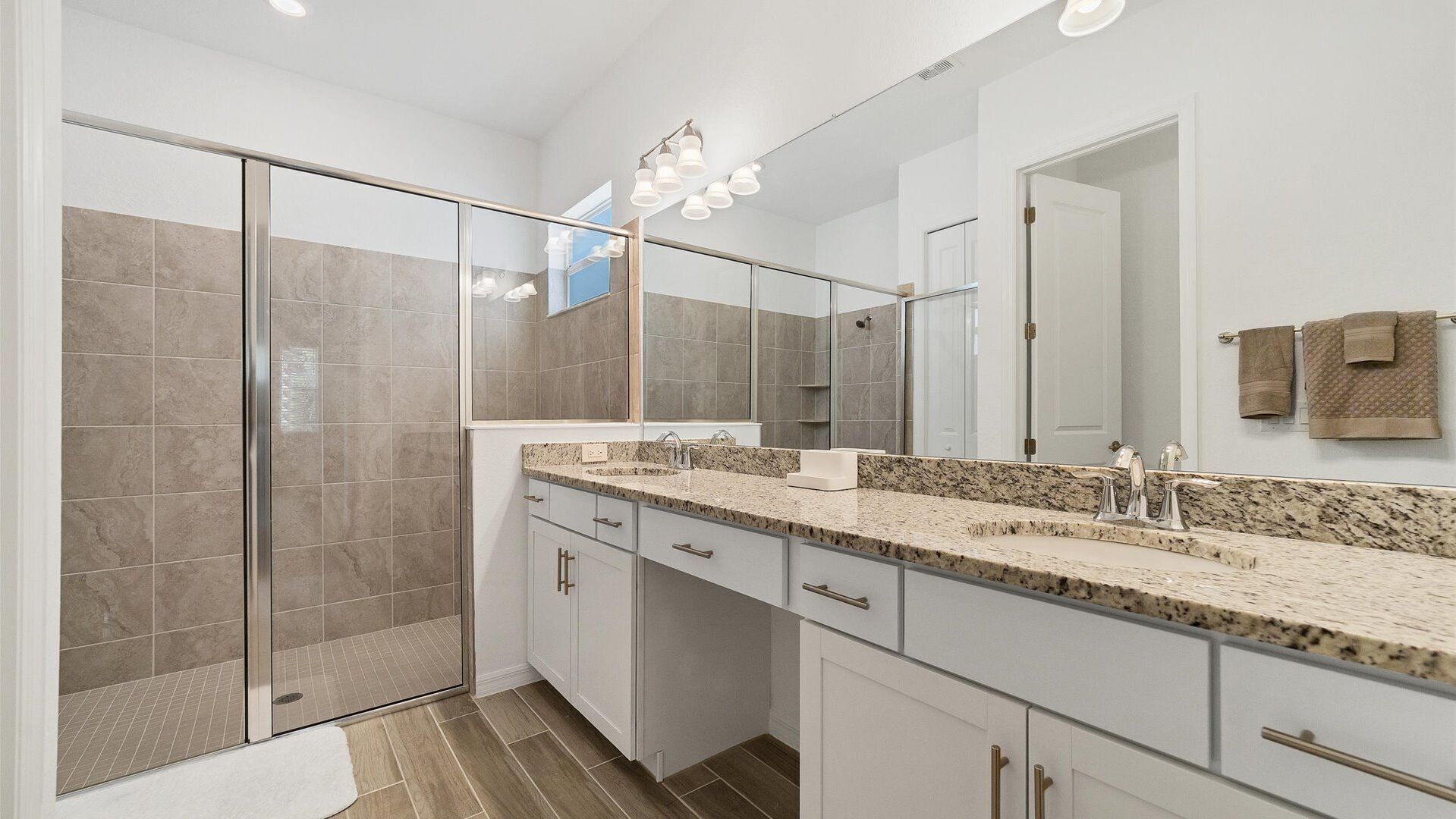 Un bagno moderno con box doccia in vetro, un ampio lavabo con piano in granito e un grande specchio.